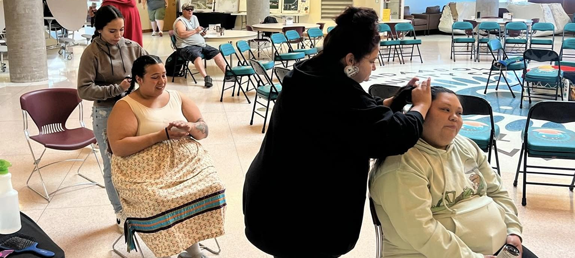 Students participating in a hands-on cultural activity, with one person styling another participant's hair in a community gathering space.